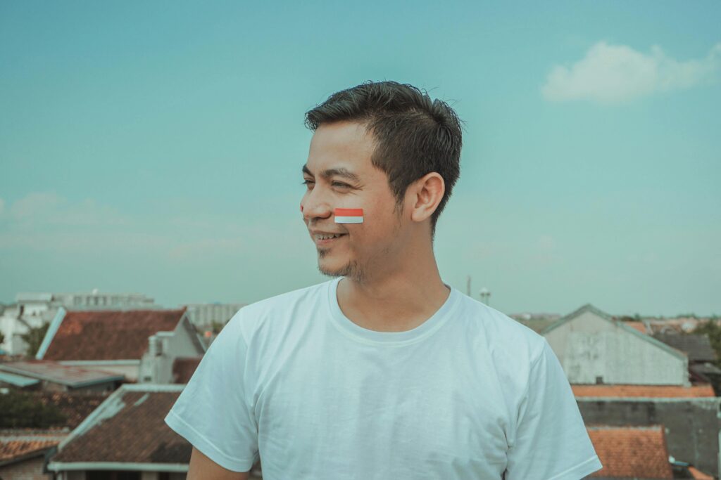 A cheerful man in a white shirt with an Indonesian flag on his cheek enjoys the sunny day in Yogyakarta.
